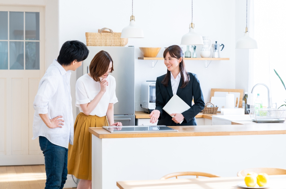 キッチンの案内をしている女性とキッチンを眺めている男性・女性の写真